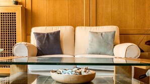 Ein modernes Wohnzimmer mit einem beigen Sofa, zwei Kissen und einem Glastisch mit einer Obstschale.