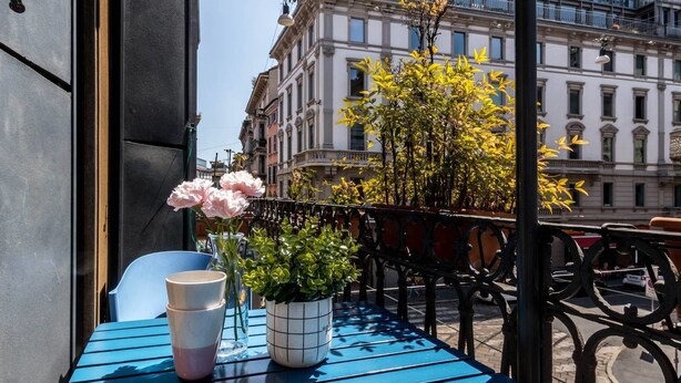 Ein blauer Tisch mit Blumen in einer Vase und einer Tasse auf einem Balkon mit Blick auf ein Gebäude.