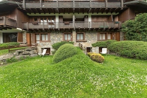 A multi-story building with stone walls, wooden balconies, and a well-maintained garden with hedges and flowers. - JOIVY Courmayeur Imperial Suite Home Plangorret (Courmayeur)