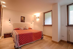 A bedroom with a large bed, two wall-mounted lamps, a window with blinds, and a radiator. - JOIVY Courmayeur Imperial Suite Home Plangorret (Courmayeur)