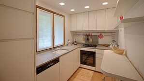 Una cocina moderna con armarios blancos, lavavajillas integrado, estufa a gas y una ventana con vidrio esmerilado.