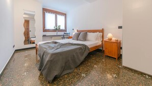 Quarto com cama, mesa de cabeceira, janela e radiador.