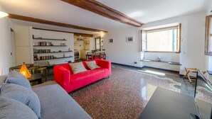 Uma sala de estar com um sofá vermelho, um sofá cinza, uma mesa de centro de madeira e uma estante.