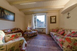 Una sala de estar acogedora con muebles de estampado floral, un ventanal con vistas a edificios y un techo con vigas de madera a la vista.