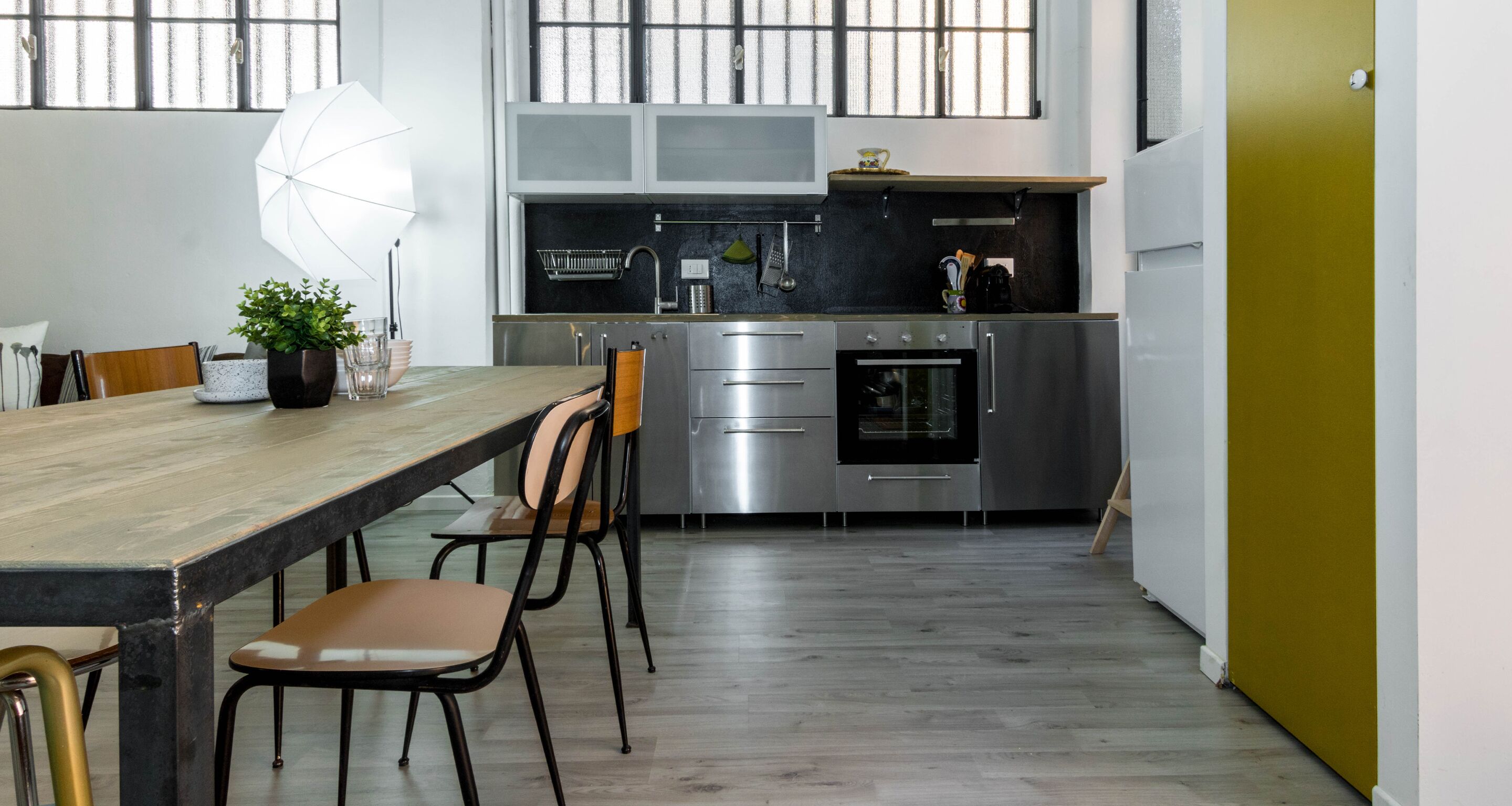 A modern kitchen with a dining area, featuring a wooden table, chairs, and a potted plant.