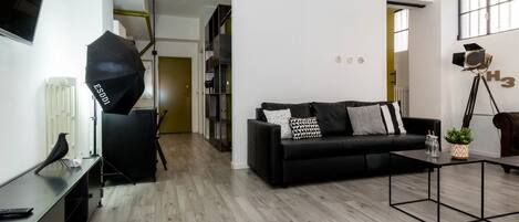 A modern living room with a black sofa, a coffee table, and a tripod with a camera on a tripod.