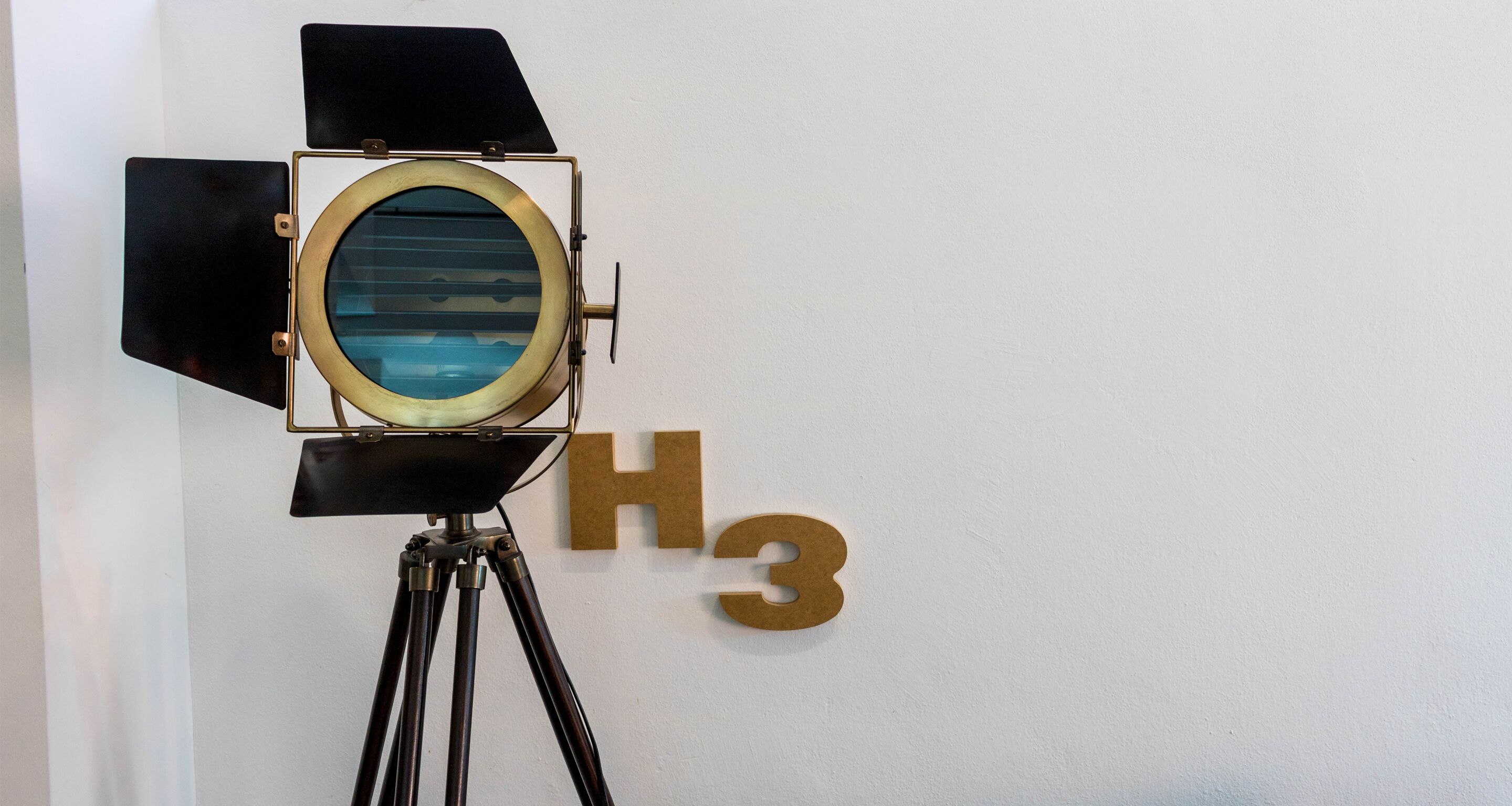 Un appareil photo ancien, posé sur un trépied, est appuyé contre un mur sur lequel on peut voir les lettres « H3 ».