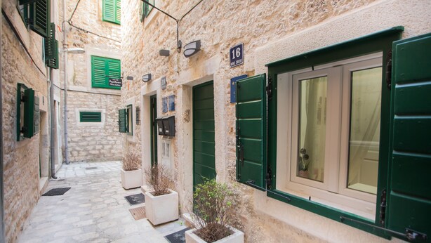 Une ruelle étroite aux murs de pierre, aux volets verts et aux portes numérotées.