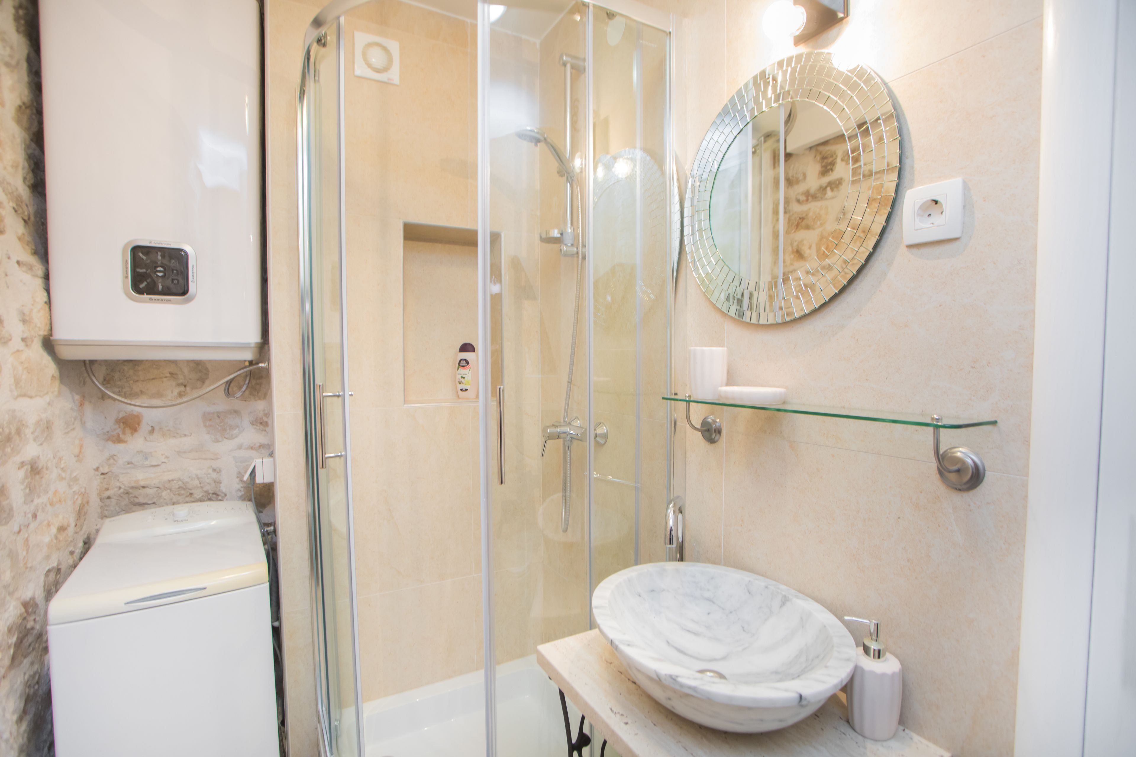 A bathroom with a glass-enclosed shower, a marble sink, and a round mirror on the wall.