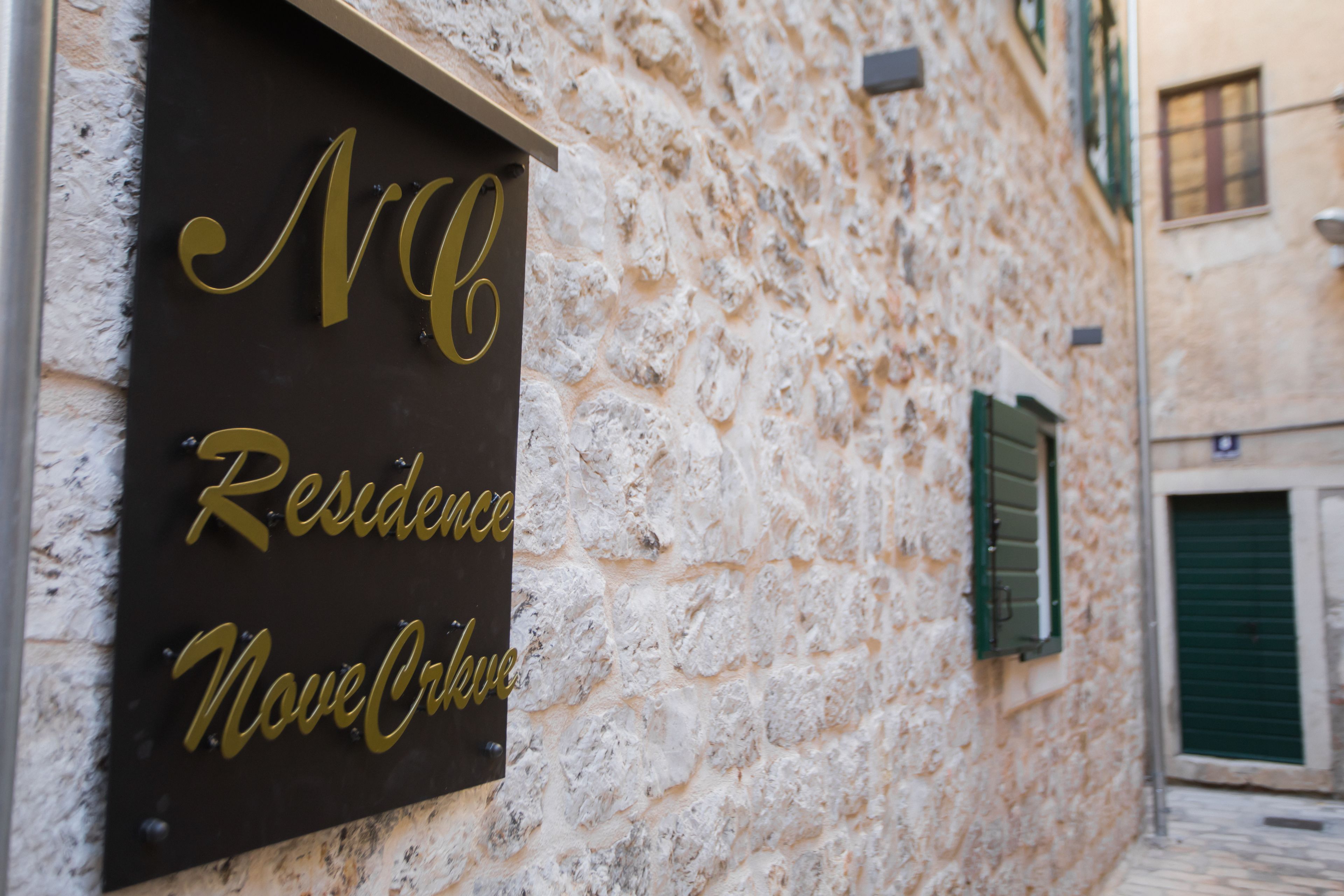 A sign with "MC Residence Nove Orizovo" on a stone wall.