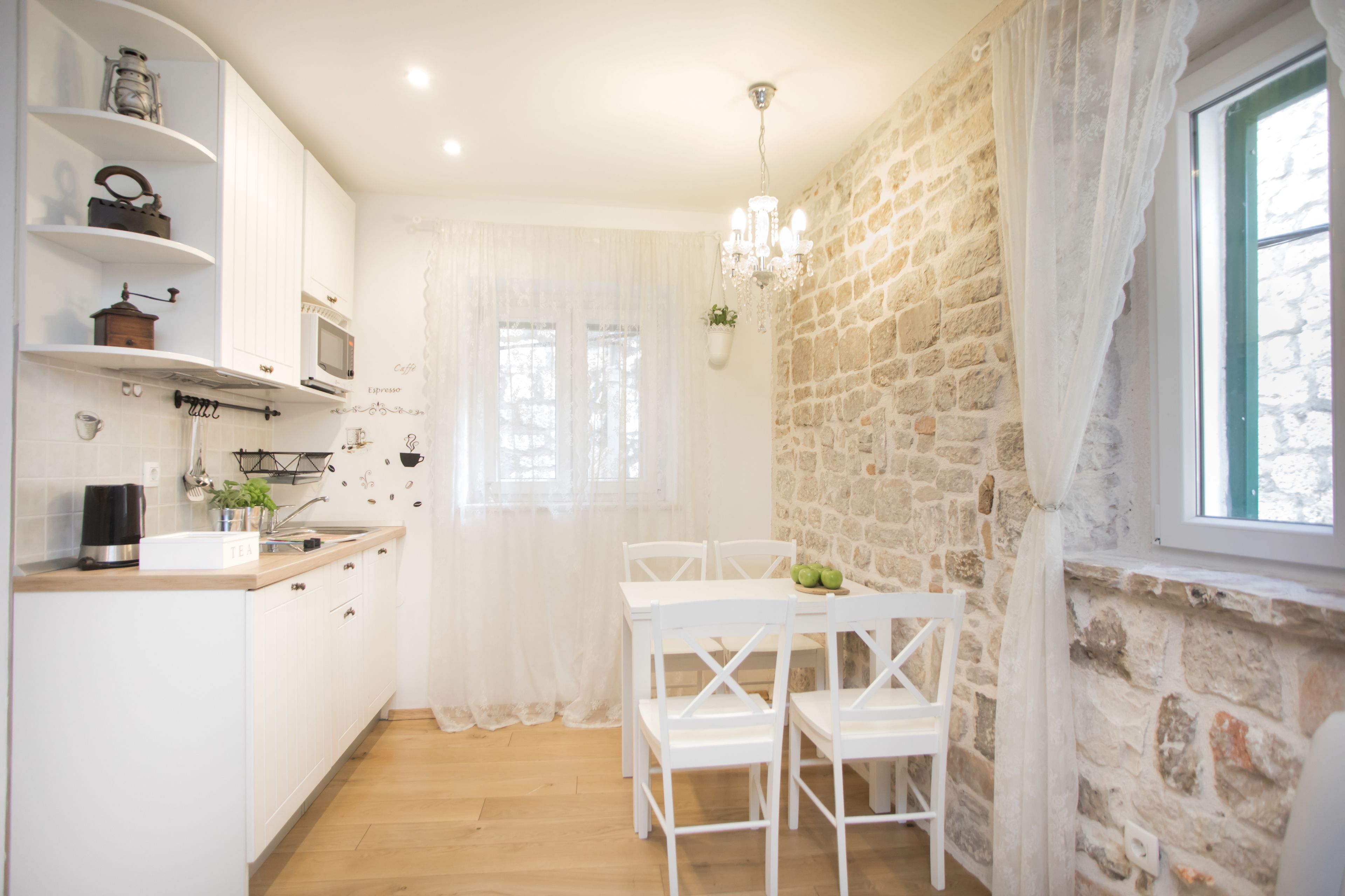 A kitchen with white cabinetry, a wooden countertop, a microwave, and a dining area with white chairs and a table.