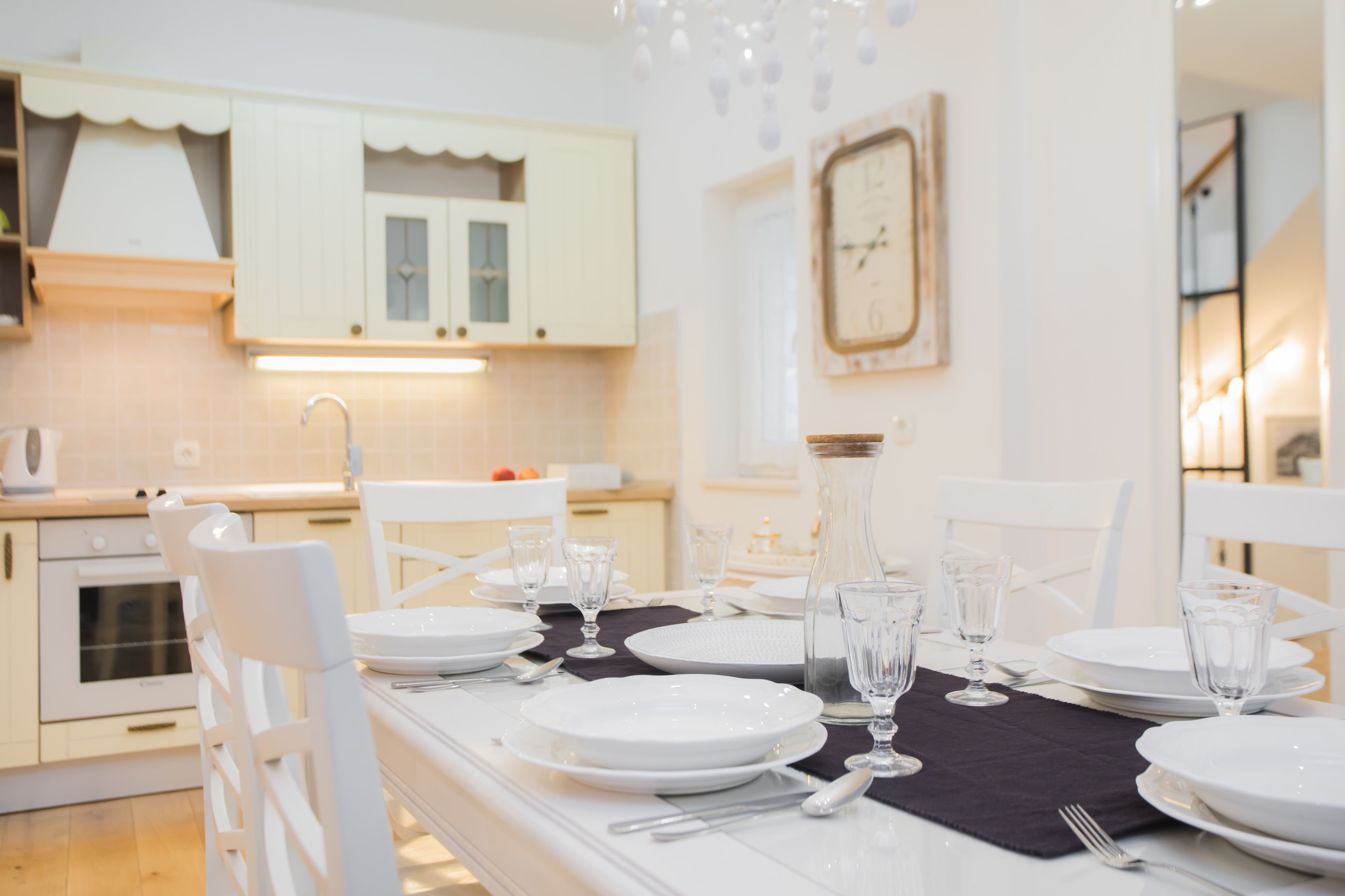A modern kitchen with white cabinetry, a dining table set for four, and a large clock on the wall.