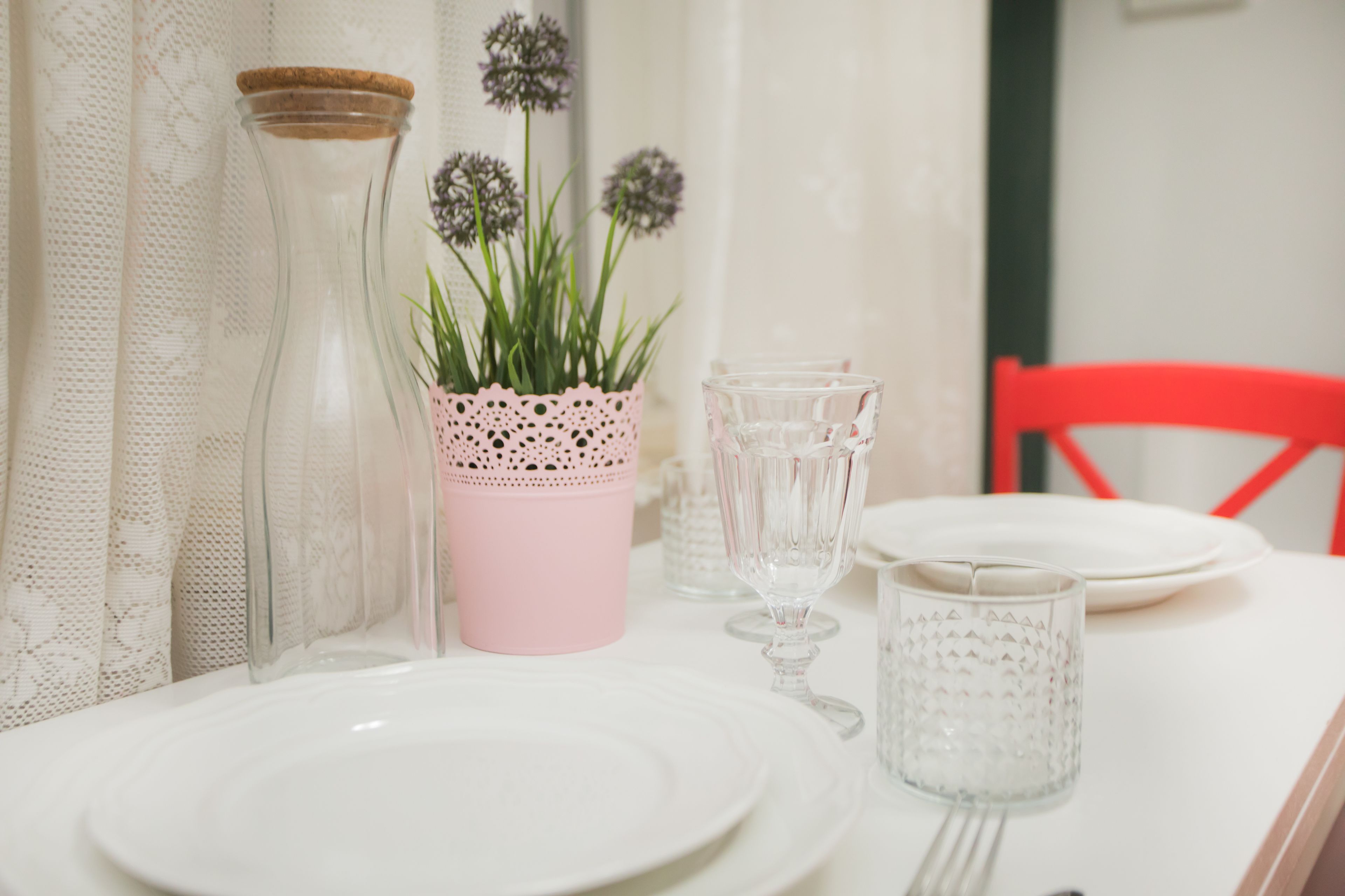 A table set with white plates, clear glassware, and a pink pot with green plants.