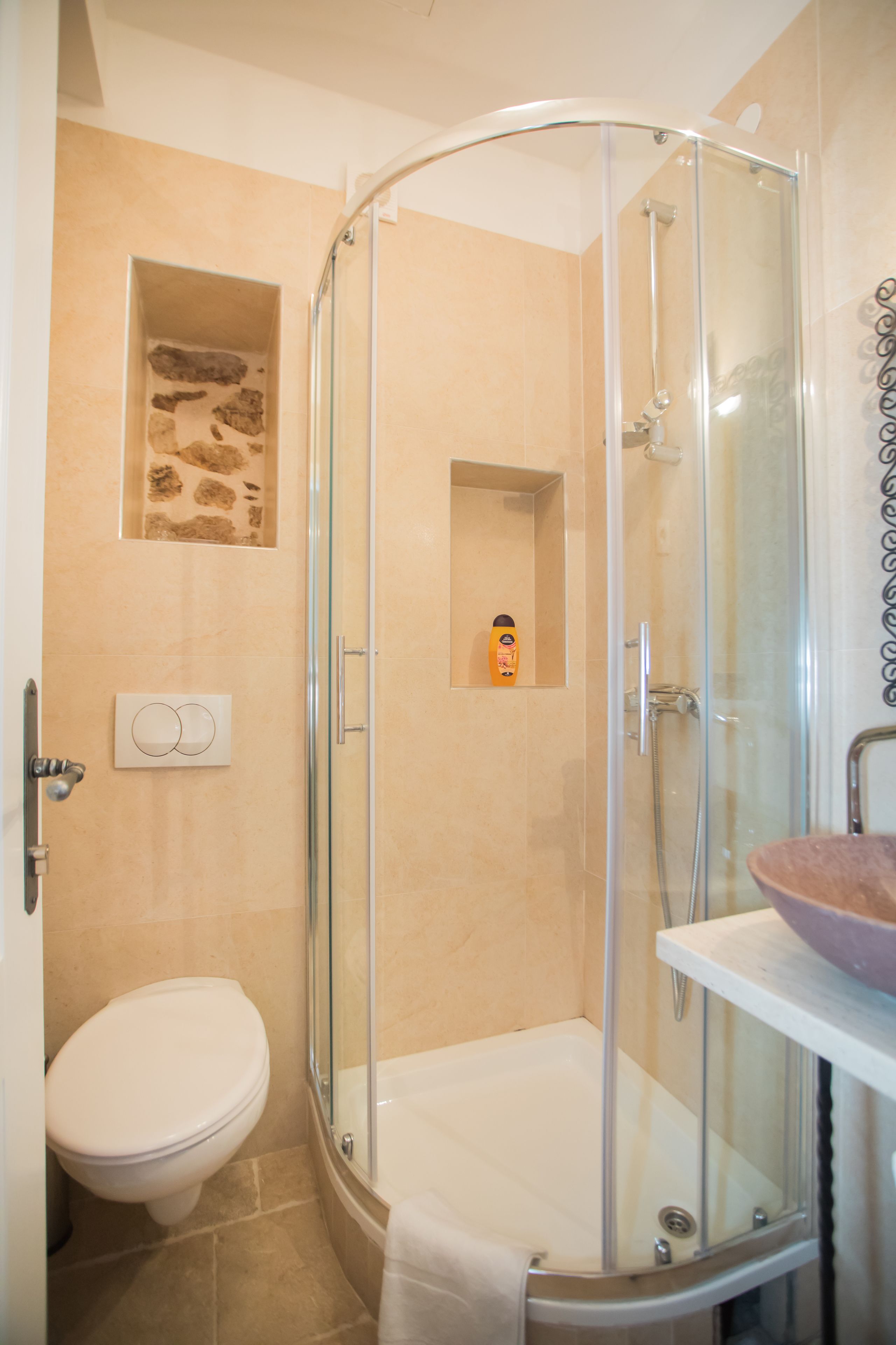 A modern bathroom with a glass-enclosed shower, a white toilet, and a beige tiled wall.