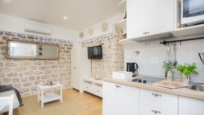 Une cuisine moderne avec des meubles blancs, un mur d’accent en pierre, un téléviseur à écran plat et une machine à café.