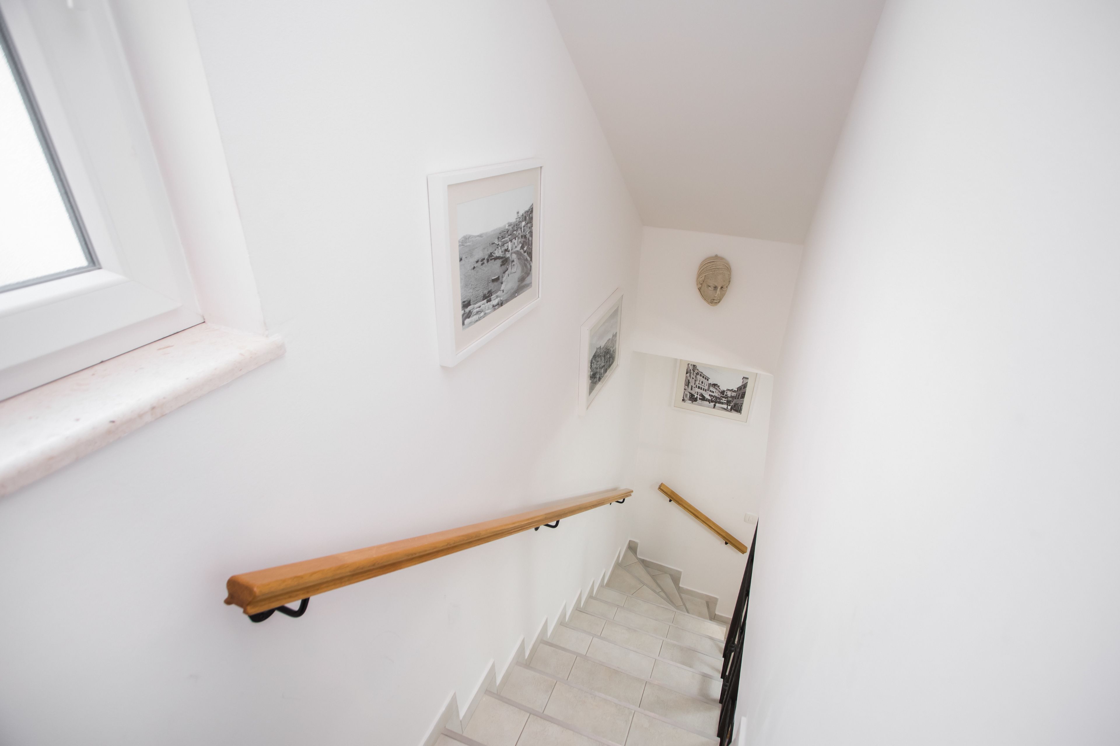 Un escalier avec des rampes en bois, des murs blancs et des tableaux encadrés.