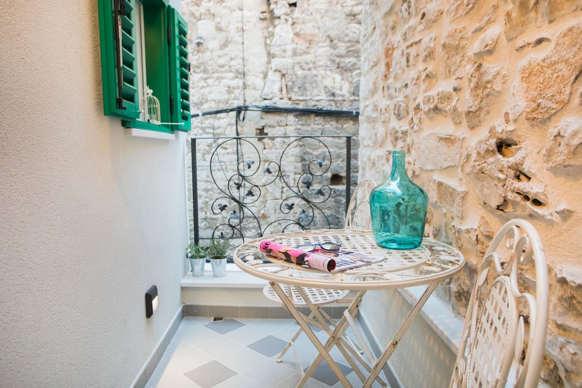 A small outdoor seating area with a round table, a green bottle, and a metal chair.