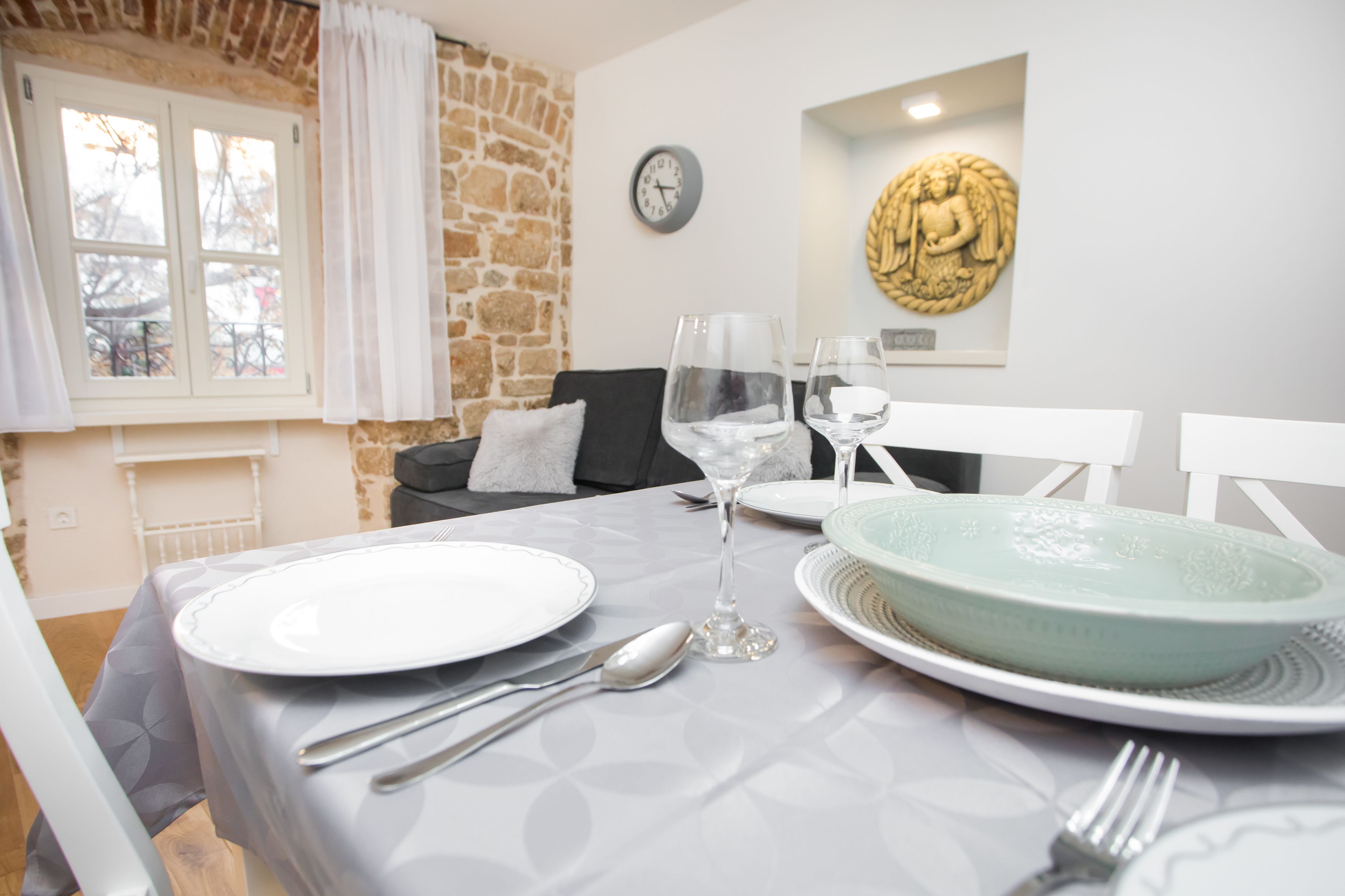 A dining table set with plates, glasses, and cutlery, a clock on the wall, and a Buddha statue.