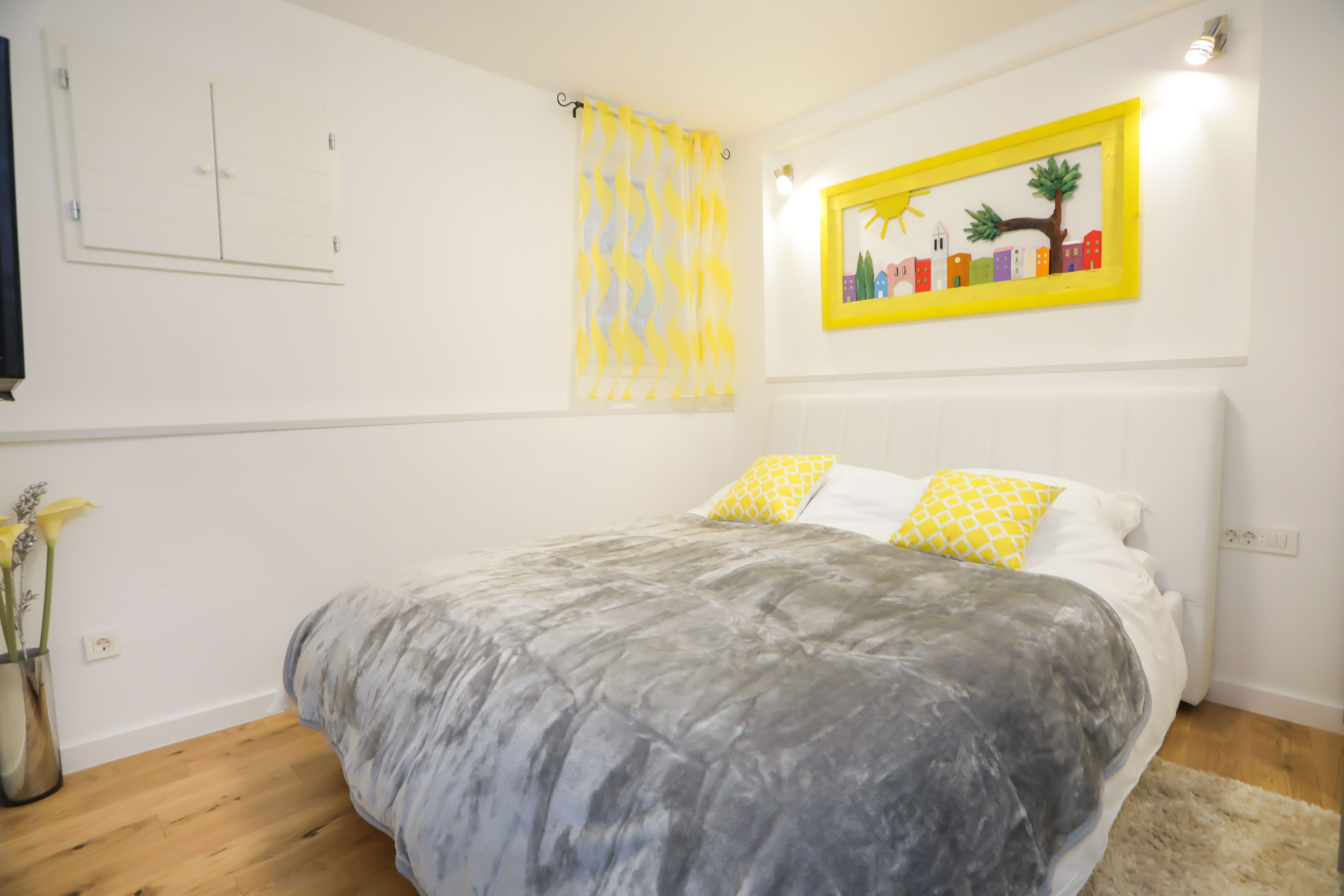 A bedroom with a bed, a wall-mounted shelf, a framed picture, and a window with curtains.
