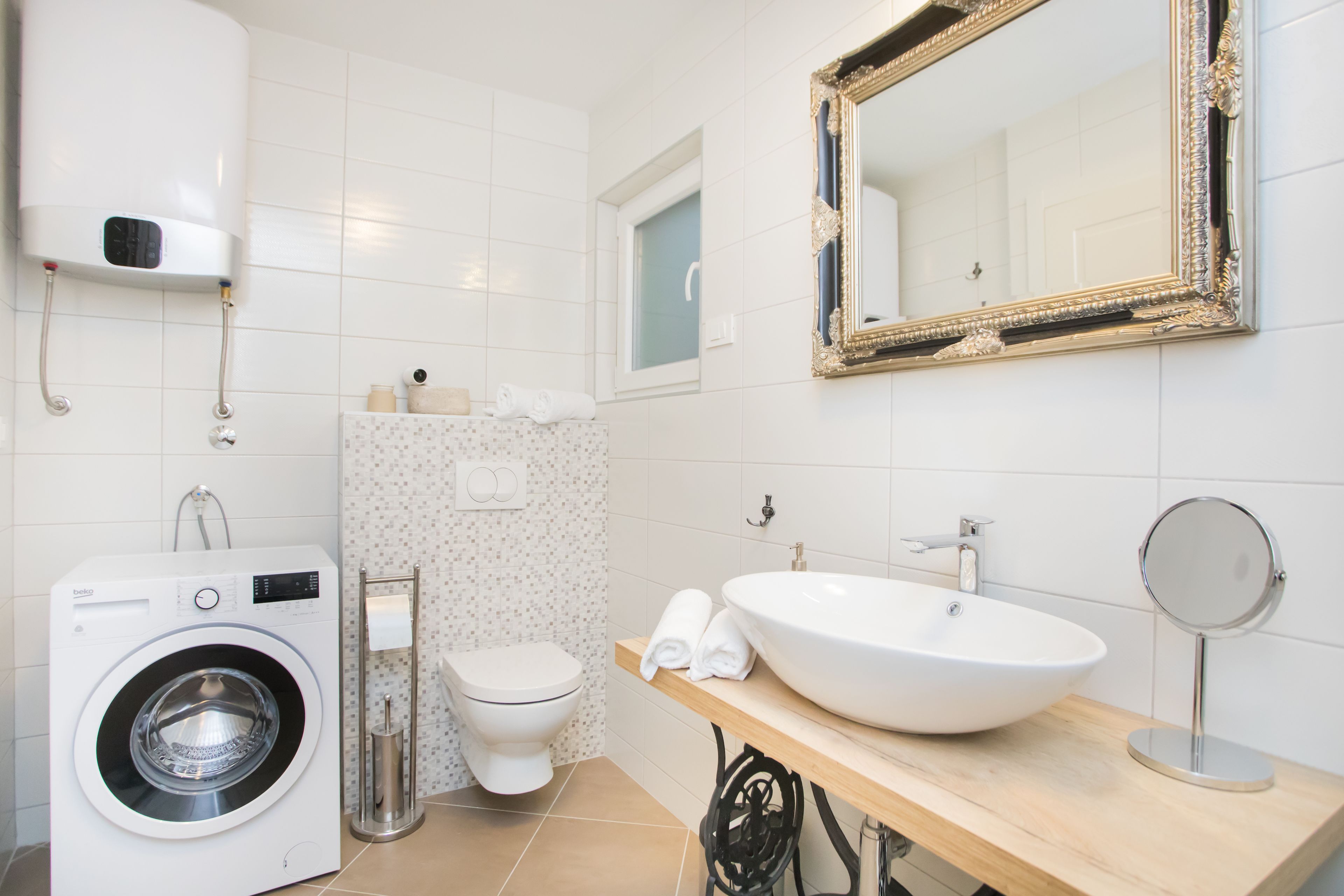 Une salle de bain moderne équipée d’un lave-linge, de toilettes, d’un lavabo et d’un grand miroir.