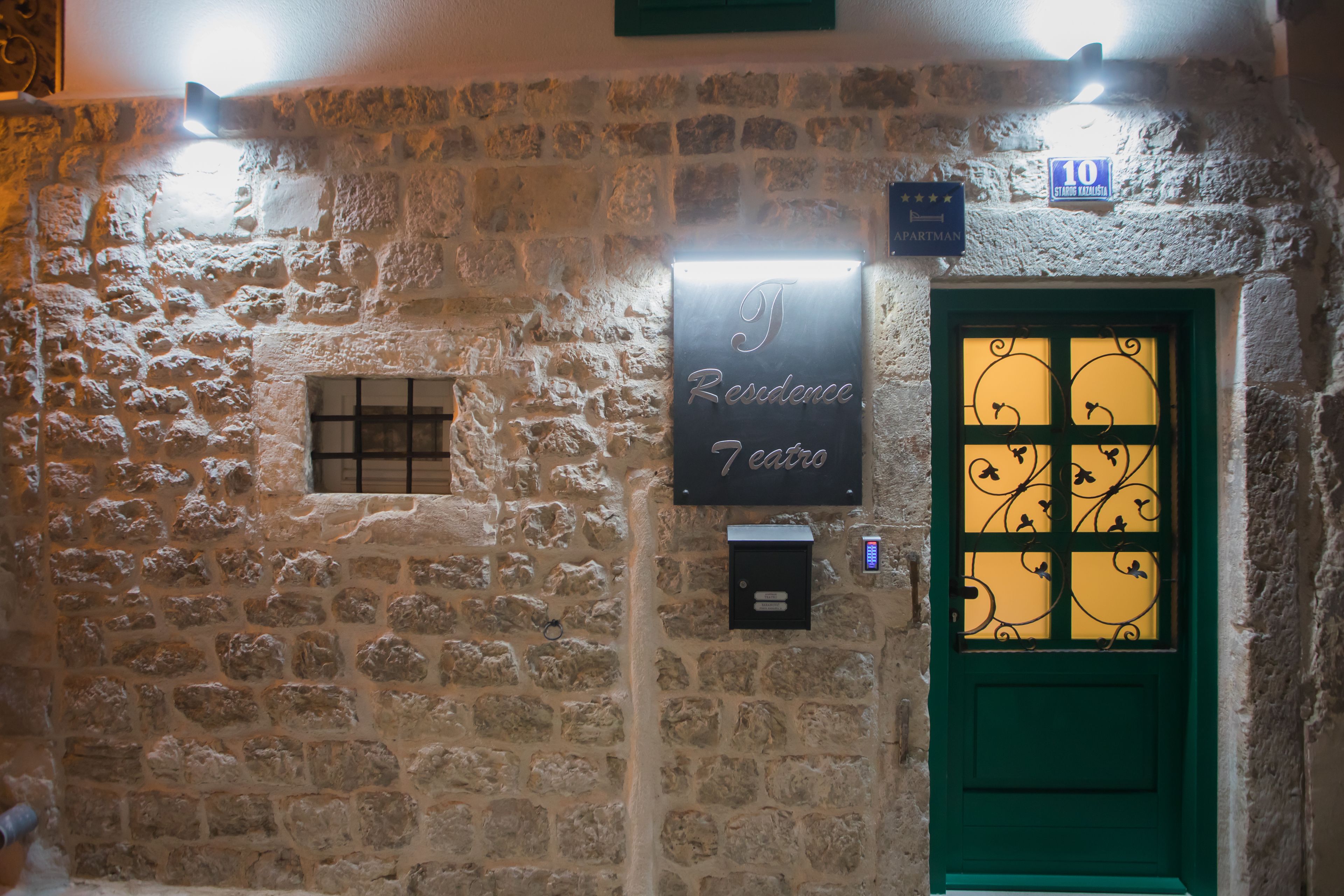 A stone wall with a green door, a sign reading "Residence 7 Carros," and a "10" sign above the door.