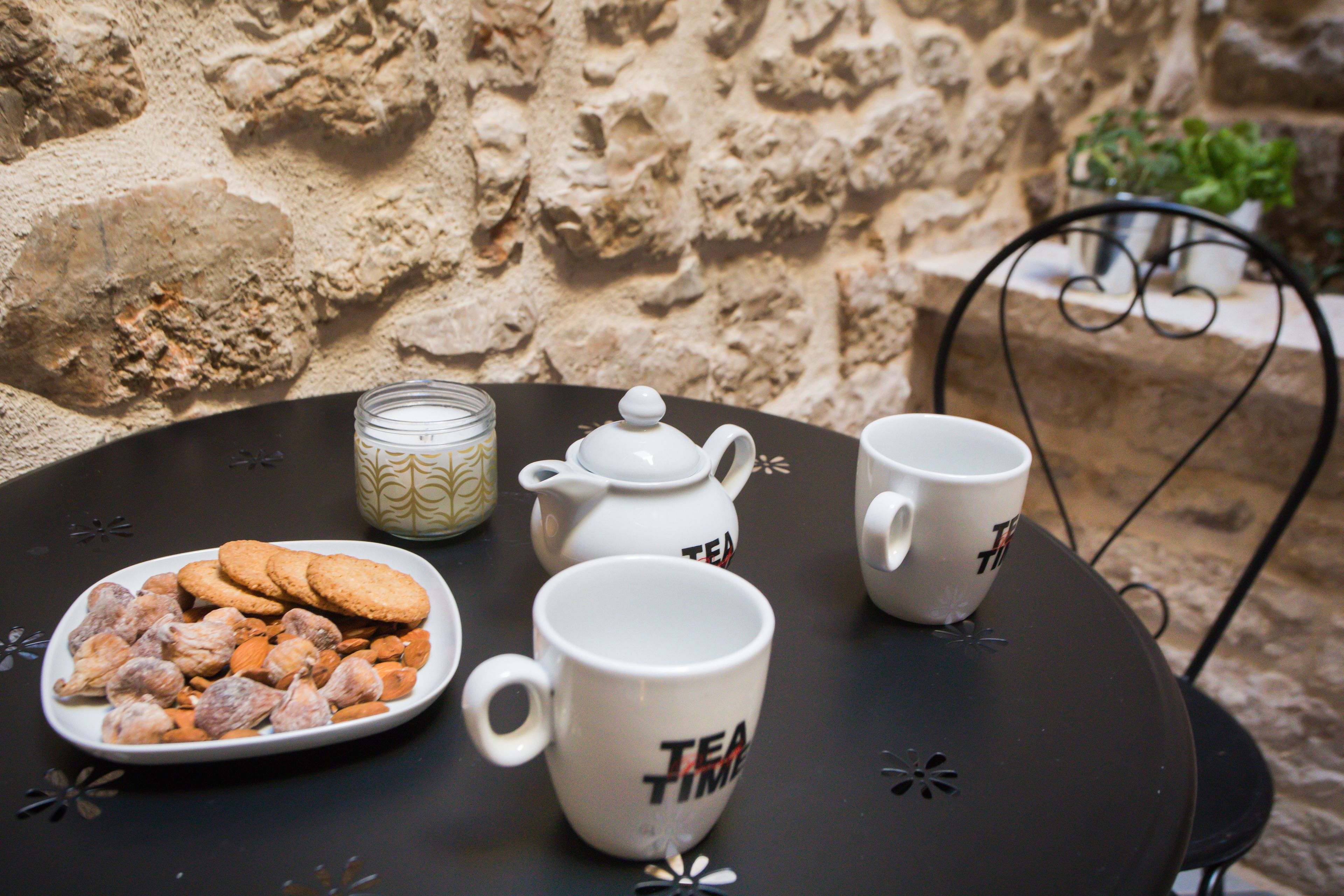 A table with a tea set, including a teapot, two cups, and a plate of cookies, set against a stone wall.