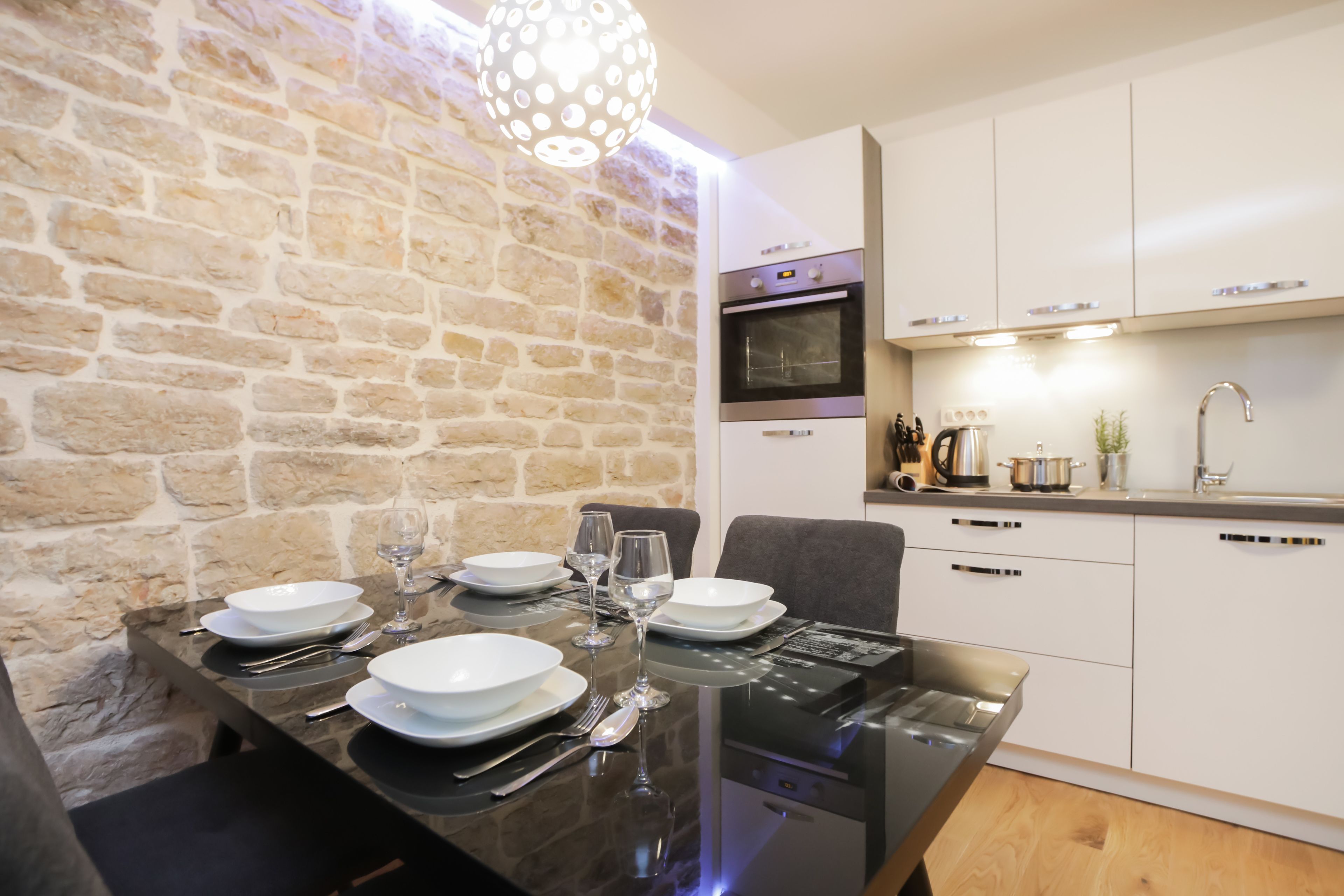 Une cuisine moderne avec des armoires blanches, un four encastré et un coin repas doté d’une table en verre pour quatre personnes.