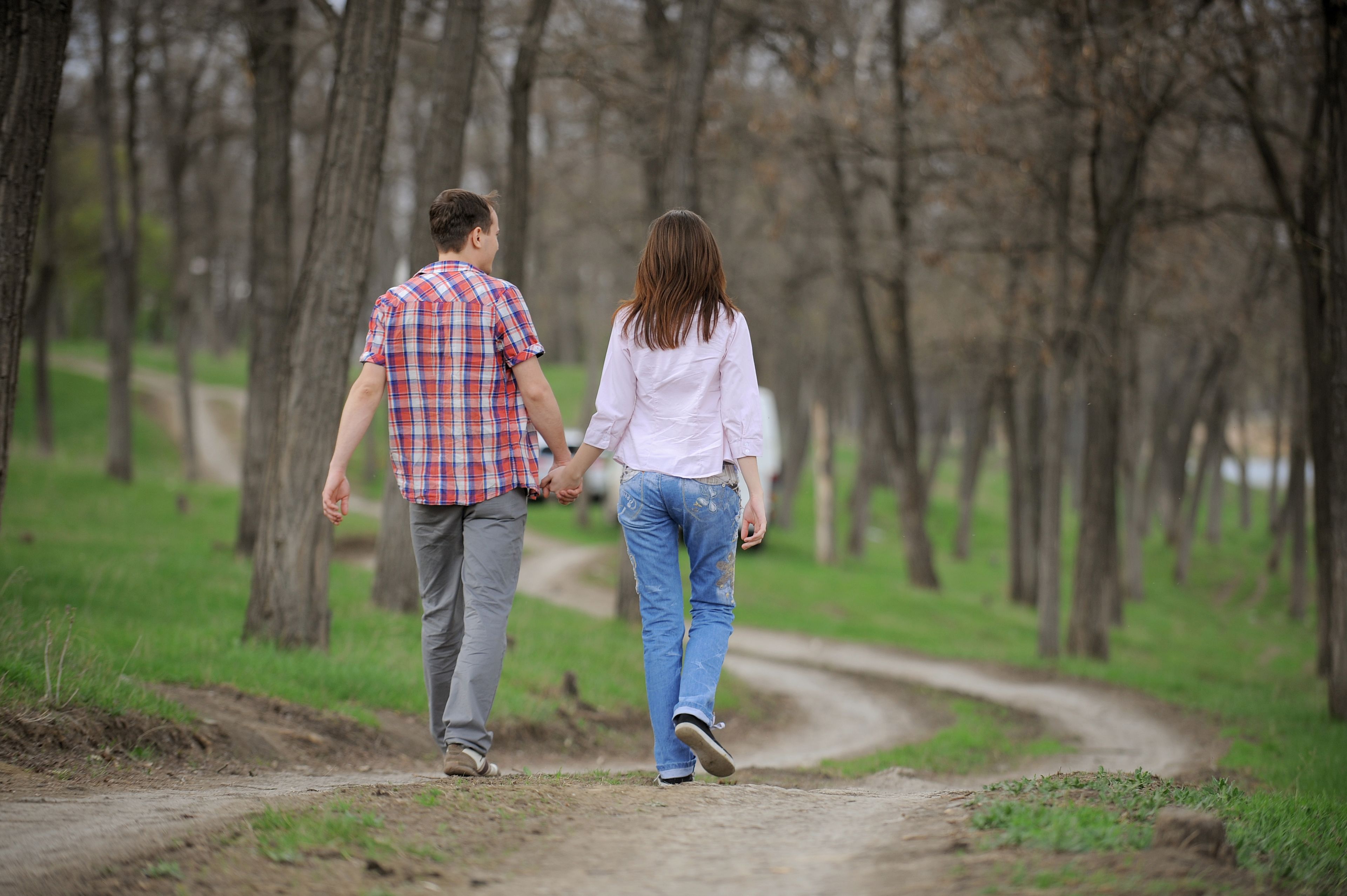 A couple walking on a dirt path in a wooded area.
