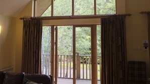 A spacious living room with a high ceiling, large windows, and a view of a wooden deck.