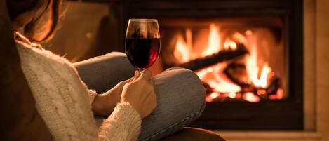 Una persona sentada en un sofá con una copa de vino tinto, frente a una chimenea.