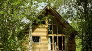 A log cabin with a balcony, surrounded by trees.