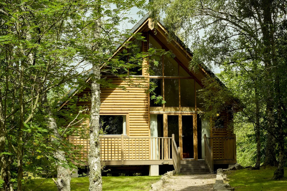 A log cabin with a balcony, surrounded by trees.
