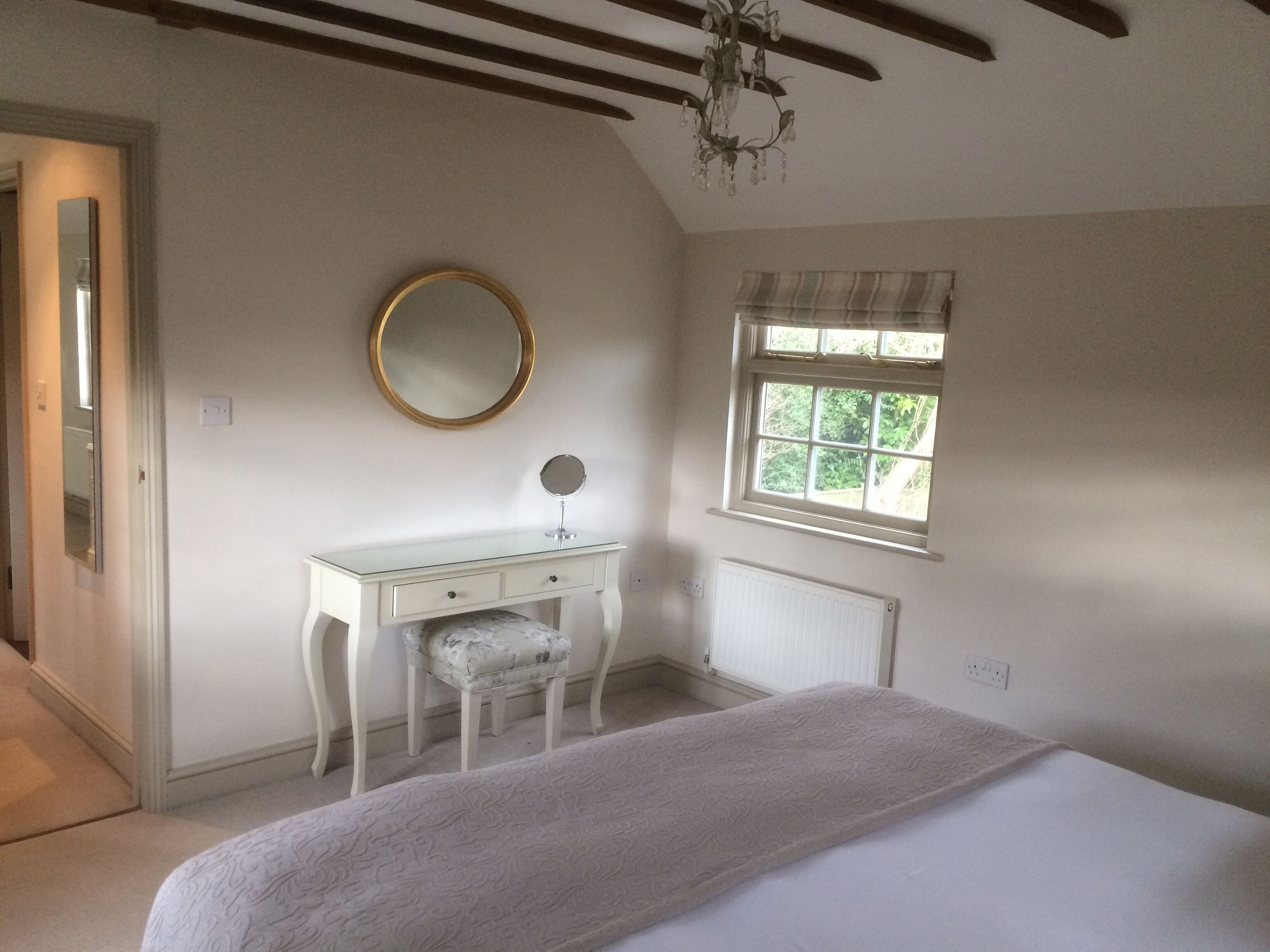 A bedroom with a bed, a dresser with a mirror, a window with curtains, and a chandelier.