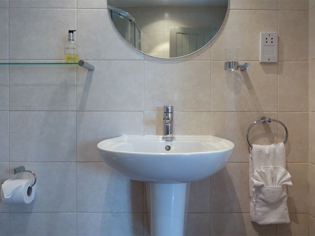 Une salle de bain avec un lavabo blanc, un miroir, un porte-serviettes et un support à papier toilette.