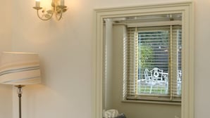 A room with a window with blinds, a lamp, and a wall-mounted light fixture. - The Barn At Woodview (Tonbridge)