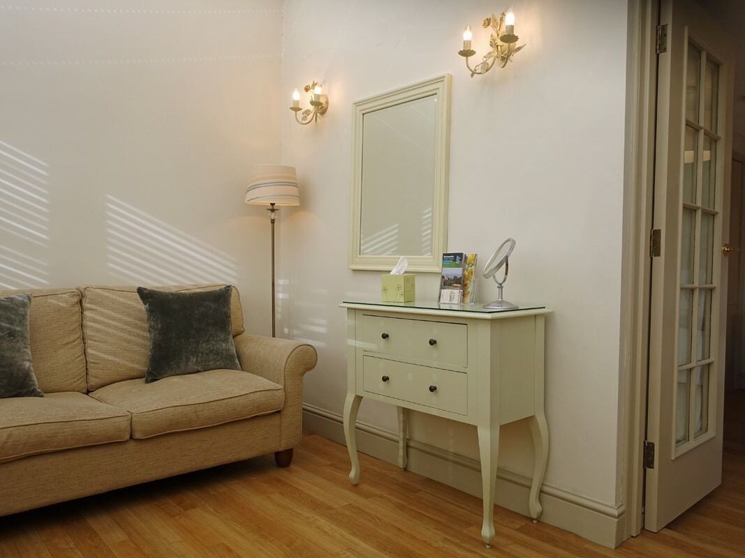 A room with a beige sofa, a white dresser with two drawers, a mirror, and wall sconces.