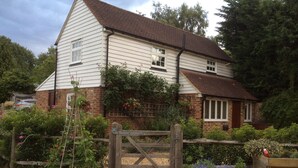 A two-story house with a brick extension, a wooden gate, and a garden with potted plants. - The Barn At Woodview (Tonbridge)