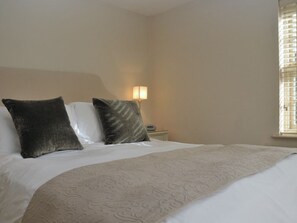 A hotel room with a bed, two pillows, a bedside lamp, and a window with blinds. - The Barn At Woodview (Tonbridge)