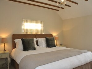 A neatly made bed with a wooden headboard, two bedside lamps, and a window with curtains. - The Barn At Woodview (Tonbridge)