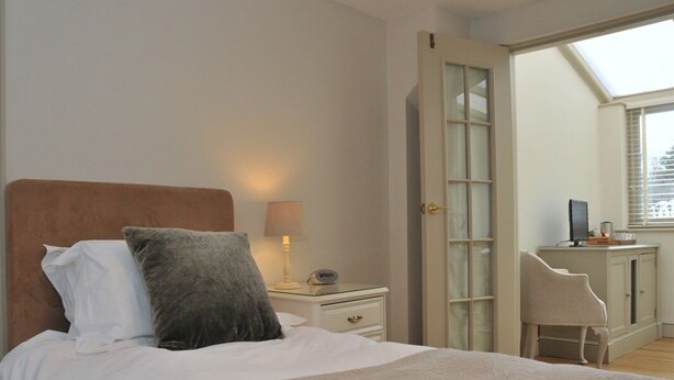 A bedroom with a bed, bedside table, lamp, and a view through an open door. - The Barn At Woodview (Tonbridge)