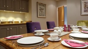 A dining table set with plates, bowls, and cutlery, with purple chairs and a framed picture on the wall. - The Barn At Woodview (Tonbridge)
