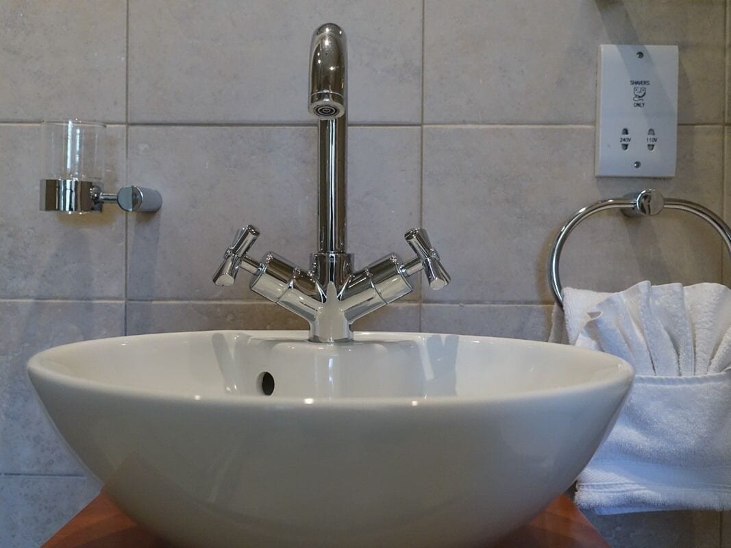 A bathroom sink with a modern faucet, a towel rack, and a power outlet on the wall.