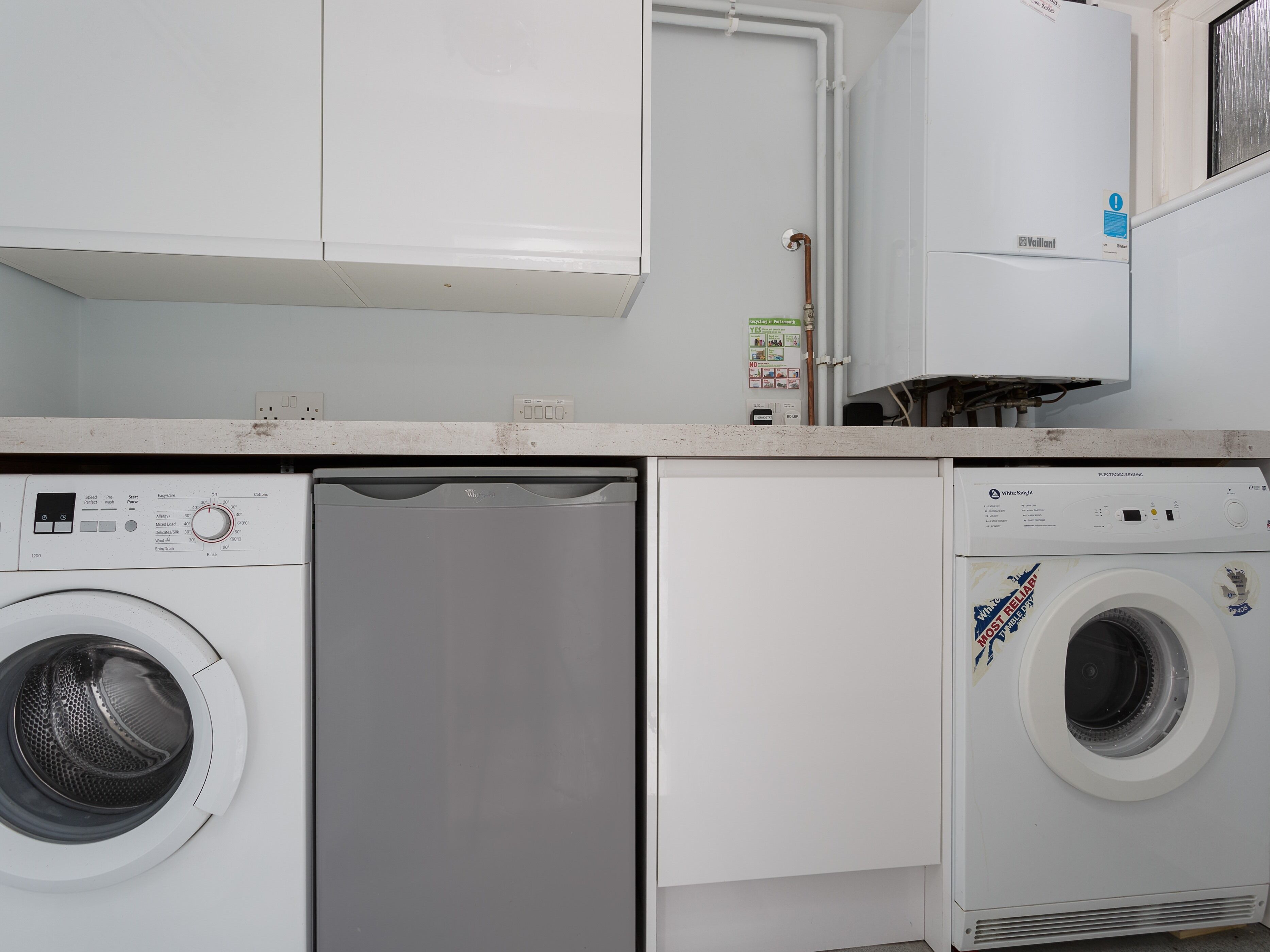 A laundry room with a front-loading washer and dryer, a white countertop, and a cabinet above.