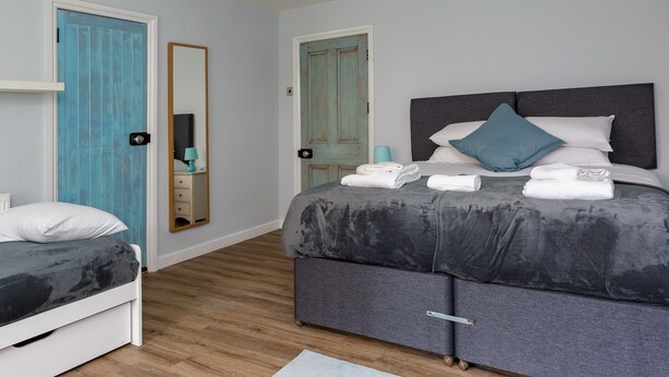 A bedroom with a bed, a bedside table, a mirror, and a door. - Albany Garden (Portsmouth)