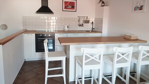 A compact kitchen with a built-in oven, a wooden countertop, and white chairs. - Jerry & Oli Apartments (Sibenik)