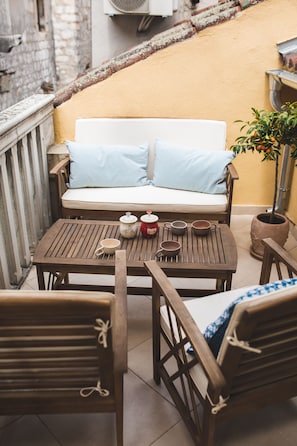 A cozy outdoor seating area with a sofa and wooden chairs, a small table with cups and a teapot, and a potted plant. - Jerry & Oli Apartments (Sibenik)