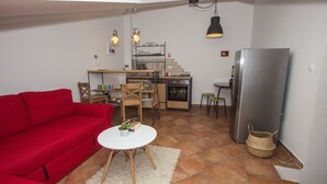 A compact living space with a red sofa, a small round table, a kitchen area with a refrigerator, oven, and a hanging light fixture. - Jerry & Oli Apartments (Sibenik)