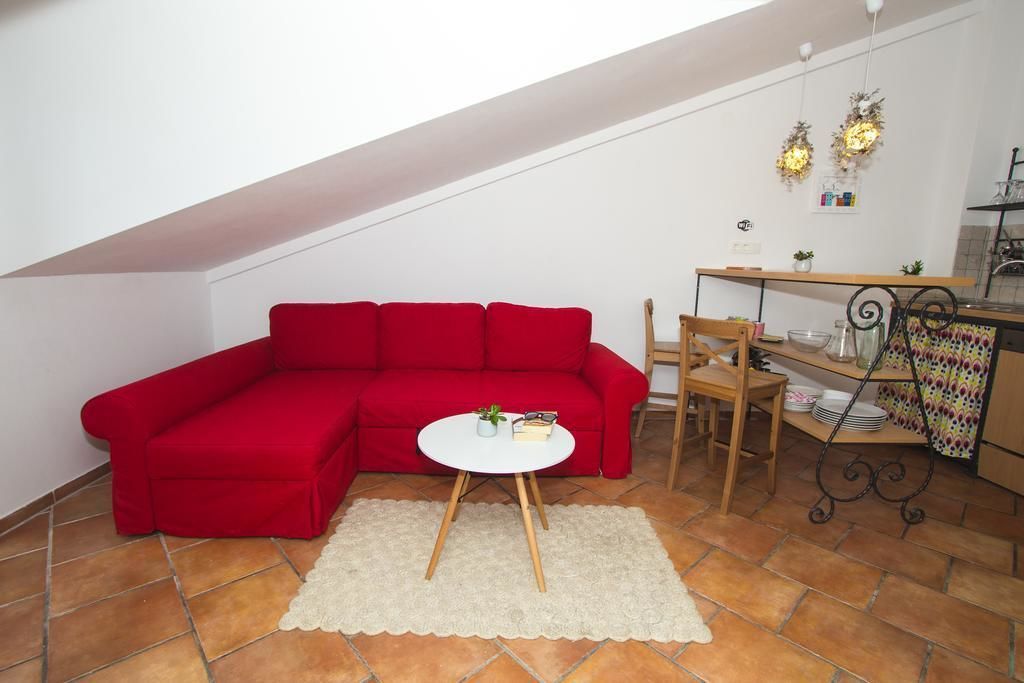 A red sectional sofa, a small white table with a plant, and a kitchen area with a shelf and a decorative wreath.