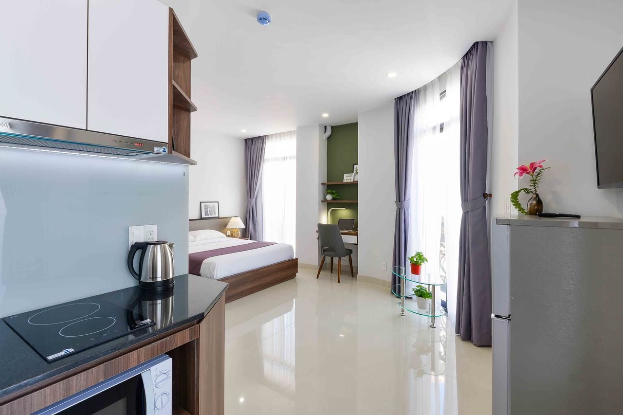 Una habitación de hotel moderna con kitchenette, una cama, un escritorio y un televisor.