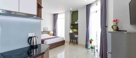 Una habitación de hotel moderna con kitchenette, una cama, un escritorio y un televisor.